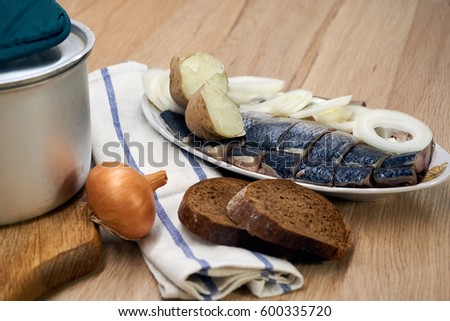Slices of herring with onion rings and rye bread on the table with fork, knife and kitchen towel.                                     