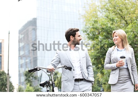 Businesspeople with bicycle and disposable cup conversing while walking outdoors Royalty-Free Stock Photo #600347057