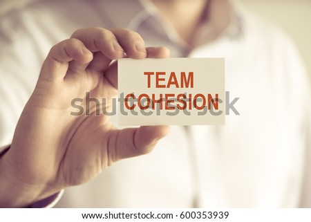 Closeup on businessman holding a card with text TEAM COHESION, business concept image with soft focus background and vintage tone Royalty-Free Stock Photo #600353939