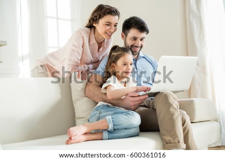 smiing parents and focused daughter using laptop at home Royalty-Free Stock Photo #600361016