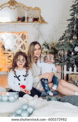 Baby girls in white dress and mother near Christmas tree