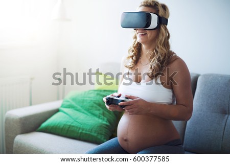 Beautiful pregnant woman having fun by playing games and using VR