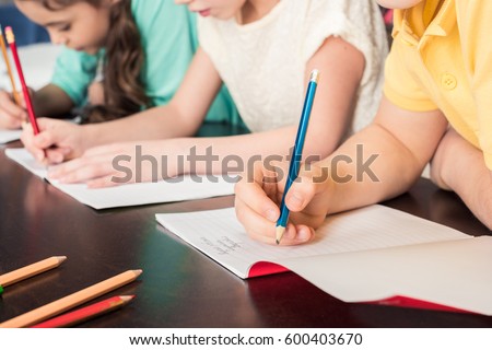 Close-up partial view of schoolchildren writing with pencils  Royalty-Free Stock Photo #600403670