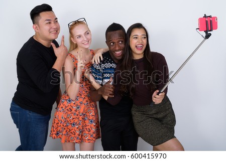 Studio shot of happy diverse group of multi ethnic friends smiling while taking selfie picture with mobile phone on selfie stick together