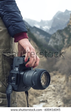 A female hand holds a camera against a mountain landscape