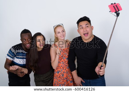 Happy diverse group of multi ethnic friends smiling while giving peace sign and taking selfie picture with mobile phone on selfie stick together