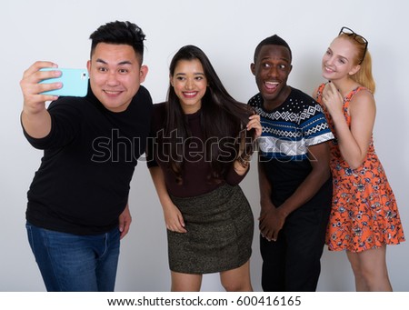 Studio shot of happy diverse group of multi ethnic friends smiling while taking selfie picture with mobile phone together