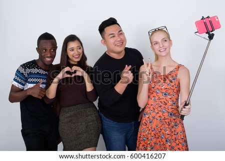 Happy diverse group of multi ethnic friends smiling and posing while taking selfie picture with mobile phone on selfie stick together