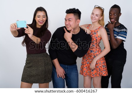 Studio shot of happy diverse group of multi ethnic friends smiling and posing while taking selfie picture with mobile phone together