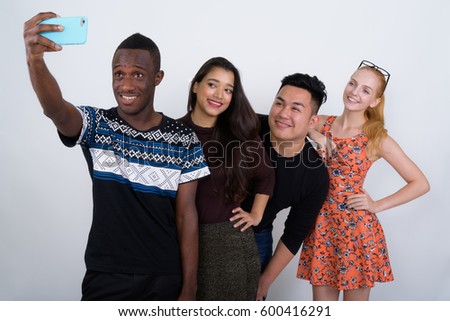 Studio shot of happy diverse group of multi ethnic friends smiling and leaning on shoulder while taking selfie picture with mobile phone together