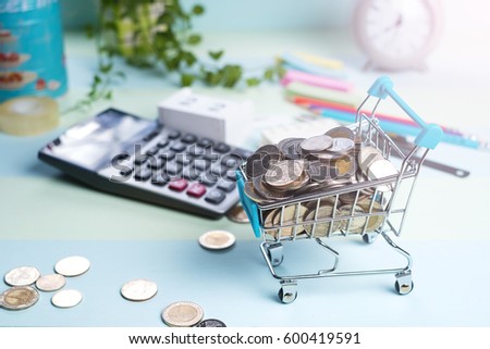 Mini shopping cart / trolley supermarket filled with coins on wood background, e-commerce, saving, online shopping and business marketing technology concept.(close up)