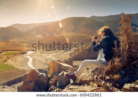 Young hiker enjoying sunset and taking picture on peak of arid mountain in Morocco valley