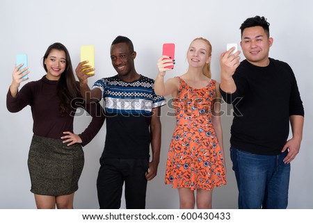 Studio shot of happy diverse group of multi ethnic friends smiling while taking selfie pictures with mobile phones together