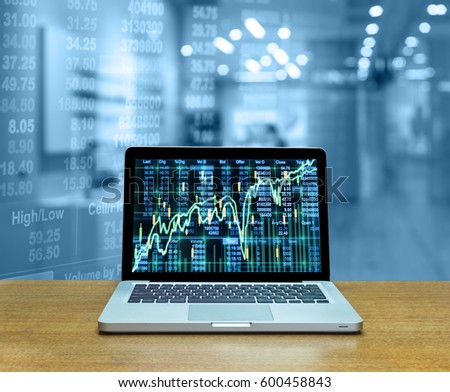 Stock exchange market trading graph over the screen of computer laptop on wood table over the photo blurred of trading graph background, business marketing trade concept