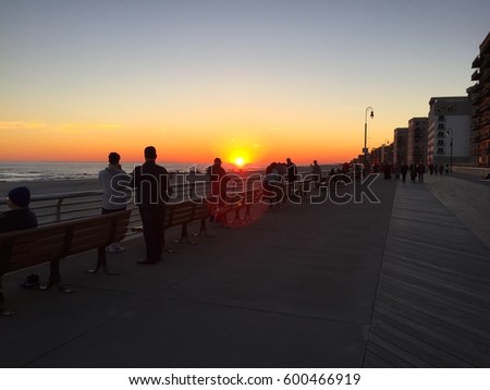 Beautiful sunset over the ocean on a coastal boardwalk town. People exercise on boardwalk stop to watch the sun set over water horizon