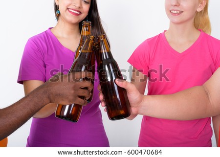 Close up of happy diverse group of multi ethnic friends smiling while cheering bottle of beer together