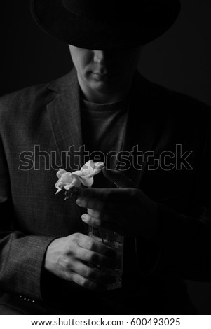 symbolic black and white image of a man in a suit and a hat with a spring white fragile flower, conceptual image of masculine protection and care