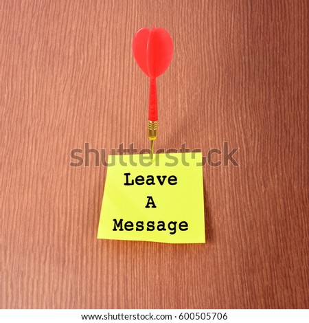 Yellow Notepad with arrow dart and text "Leave A Message". Wooden background