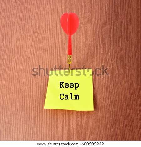 Yellow Notepad with arrow dart and text "Keep Calm". Wooden background