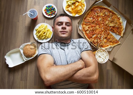 Unhealthy concept. beautiful athletic guy with unhealthy food: pizza, lemonade, chips, candy and chips.