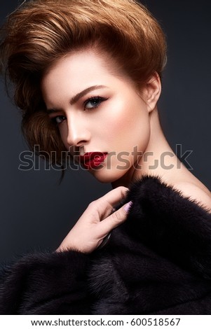 Young girl in a fur coat and bright makeup. Beautiful model with red lips and hairstyle. Photo is taken in a studio. Beauty of the face.