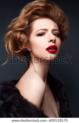 Young girl in a fur coat and bright makeup. Beautiful model with red lips and hairstyle. Photo is taken in a studio. Beauty of the face.