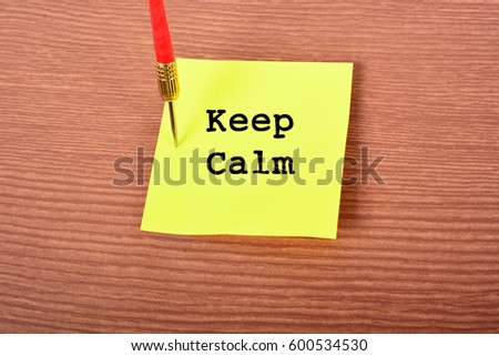 Yellow Notepad with arrow Dart and text "Keep Calm". Wooden background