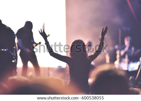Rear view of a woman with arms outstretched at concert