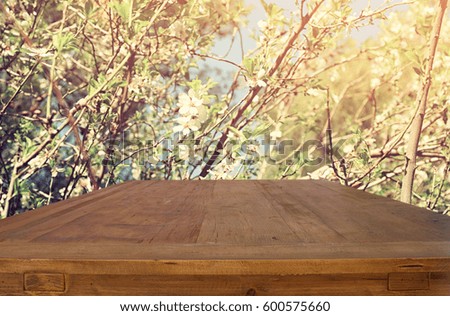 wooden rustic table in front of spring white cherry blossoms tree. vintage filtered image. product display and picnic concept