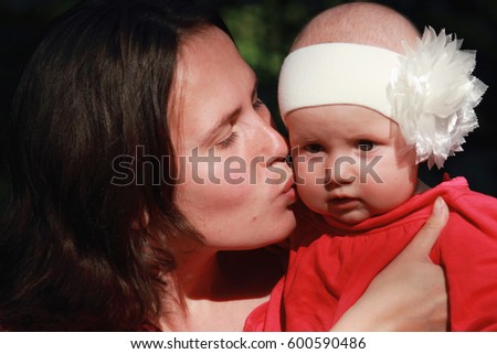 Parents love.  Happy young mother kissing her beautiful baby girl. Beautiful baby girl sitting in mom's arms.