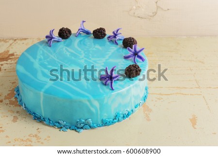 Modern trendy mousse cake with blue marble mirror glaze. Flowers and blackberries decor. Selective focus. Space for text, wooden background.