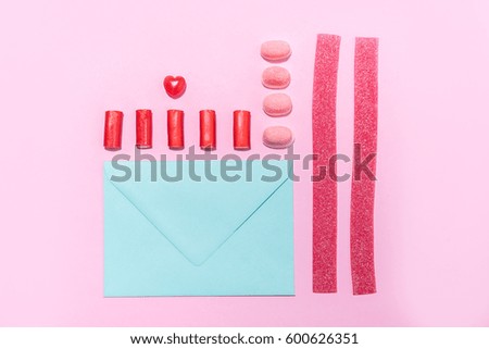 Picture of jelly sugar candies and lollies in a row with blank paper envelope over pink background
