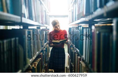 Reading a book in library. Young attractive librarian reading a book between library bookshelves