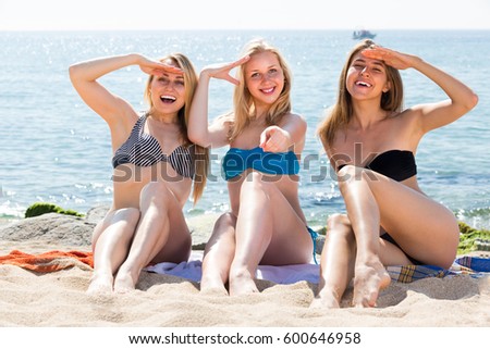 three cheerful  smiling girls in bikini relaxing on sandy beach on sunny day 
