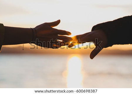 Sun shines behind hands of man and woman reaching fingers to each other Royalty-Free Stock Photo #600698387