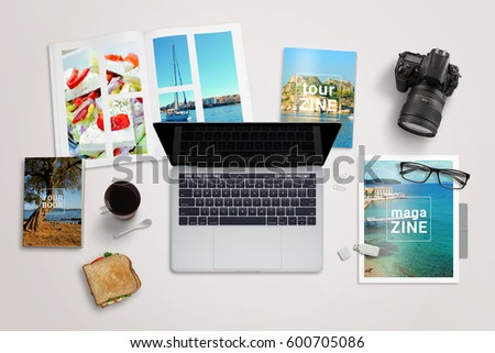 Journalist or reporter writing desk. Laptop surrounded by magazines. Camera, coffee, sandwich, memory stick; glasses beside. Top view. Royalty-Free Stock Photo #600705086