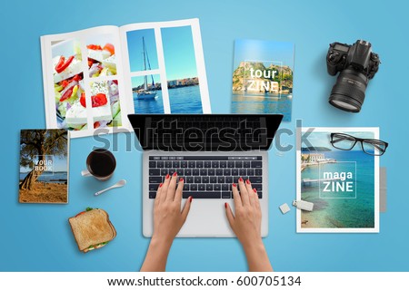 Travel agency work desk. Woman typing on laptop computer with blank screen for mockup. Travel magazines beside. Top view.