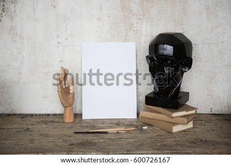 White mock up paper art board with wooden hand, pile of books and black mannequin head. Empty canvas with copy space for text. Template for your content. Hipster background, creative concept