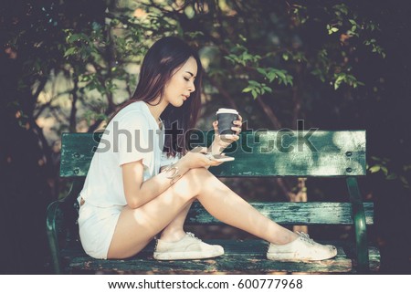 Outdoor portrait of pretty woman playing game on mobile phone and holding a cup of coffee in the park. life style, vintage style. Royalty-Free Stock Photo #600777968