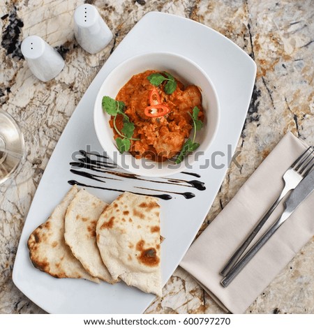 Chicken fillet slices fried in spicy cream sauce with tortilla bread served in white bowl with glass of wine, knife and fork on napkin on marble table