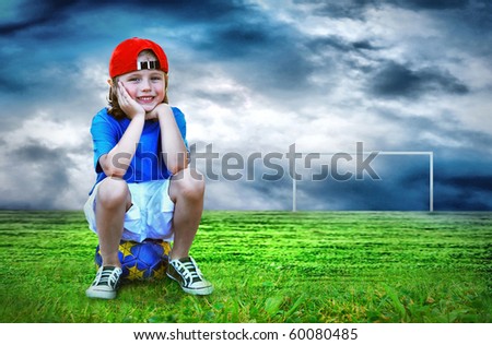 Young boy seating on the ball in green field