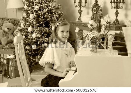 Beautiful, elegant little girl holding hands on the keys of a white Grand piano. Girl playing at the Christmas concert in the music school.Black-and-white photo. Retro style.