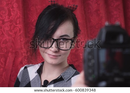 A young female blogger shoots himself on camera, cute brunette, hipser glasses, lifestyle vlog, red background