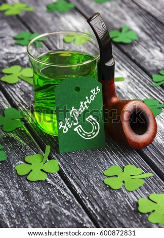 St Patrick's Day background, Glass with Green Irish beer, clover shamrock, Greeting card with text "St Patrick and horseshoe"?� and   tobacco Pipe on a wooden desk background. Side view
