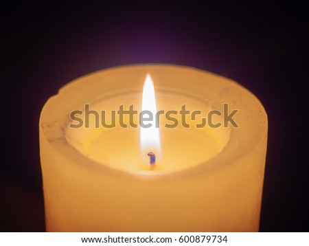 Large, burning, wax candle on a dark background with flaming, burning fuse, close-up photo with soft, blurred focus.
