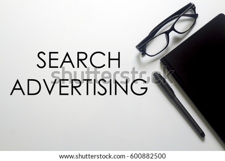 A glasses, notebook and pen with SEARCH ADVERTISING written on white background. A business concept.