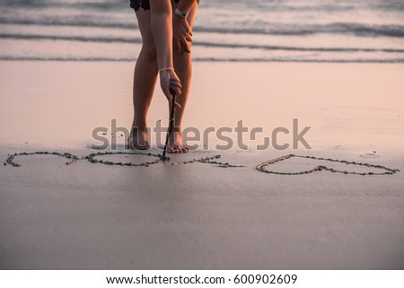 Woman relaxing on the beach by writing Love You on the sand, holiday concepts.
