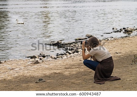 The girl is taking pictures of a swan on the river bank. Prague.
