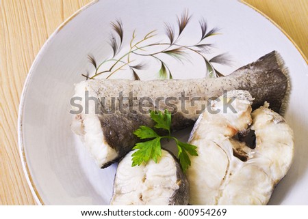 Pieces of hake with parsley on the plate on wooden background