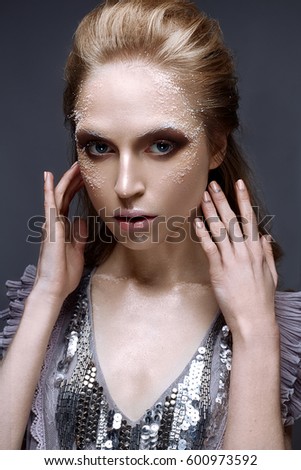 Young girl with creative makeup and textures on her face. Beautiful model in a lilac dress with sparkles. Photo is taken in the studio. Beauty of the face.